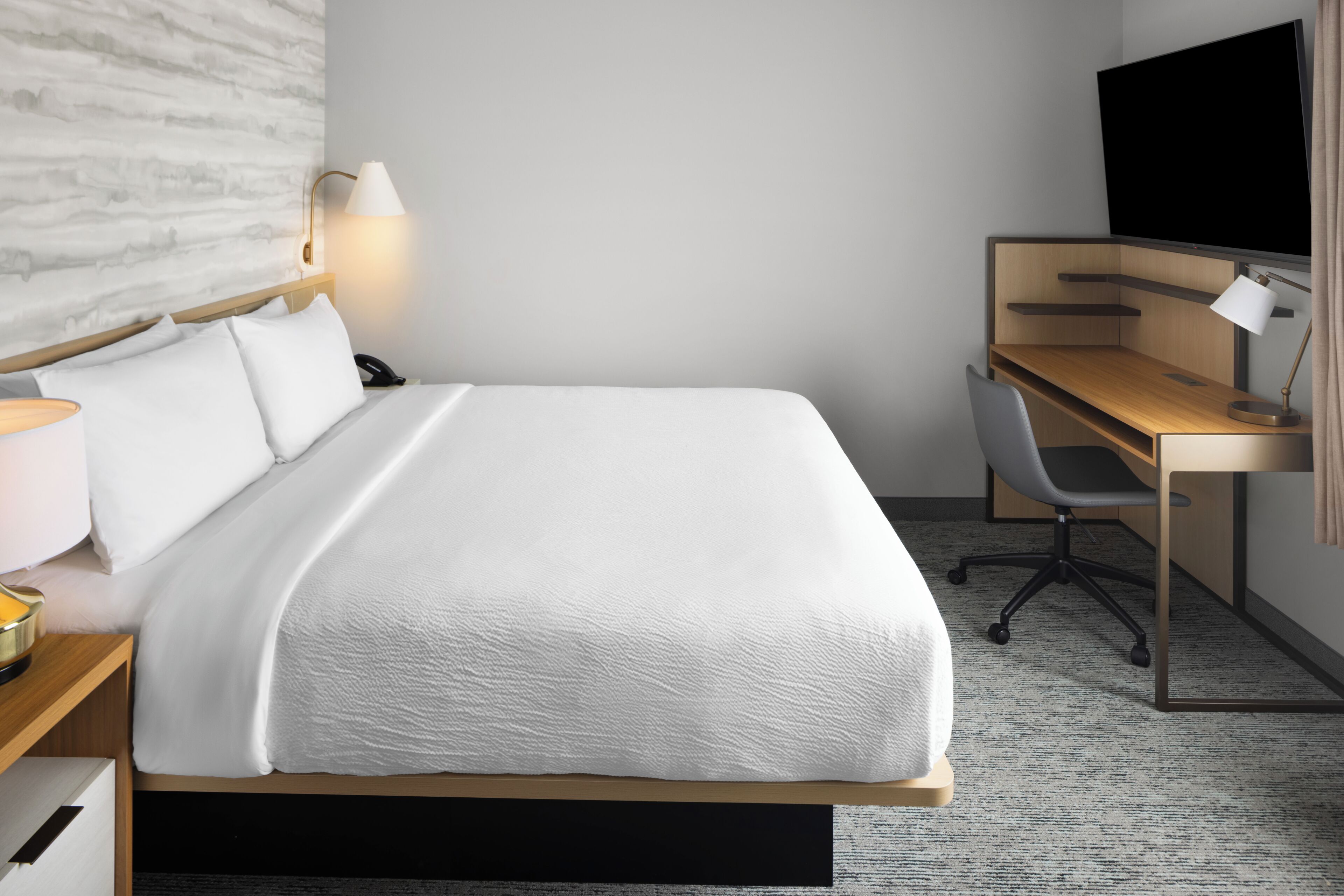 Una habitación de hotel con cama, escritorio, silla, lámpara y televisión.