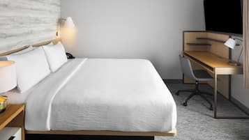 Una habitación de hotel con cama, escritorio, silla, lámpara y televisión.