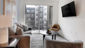 A modern living room with a sofa, armchair, coffee table, and a TV mounted on the wall. - Landing | Stunning 1BD, Gym, Yoga Studio (Huntsville)