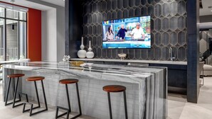 A modern kitchen with a marble island, bar stools, a large TV, and decorative vases. - Landing | Spectacular 1BD, Yoga Studio, Gym (Huntsville)