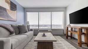 A modern living room with a grey sofa, a wooden coffee table, and a large window with blinds. - Landing | Amazing 1BD, Game Room, Yoga Studio (Hartford)