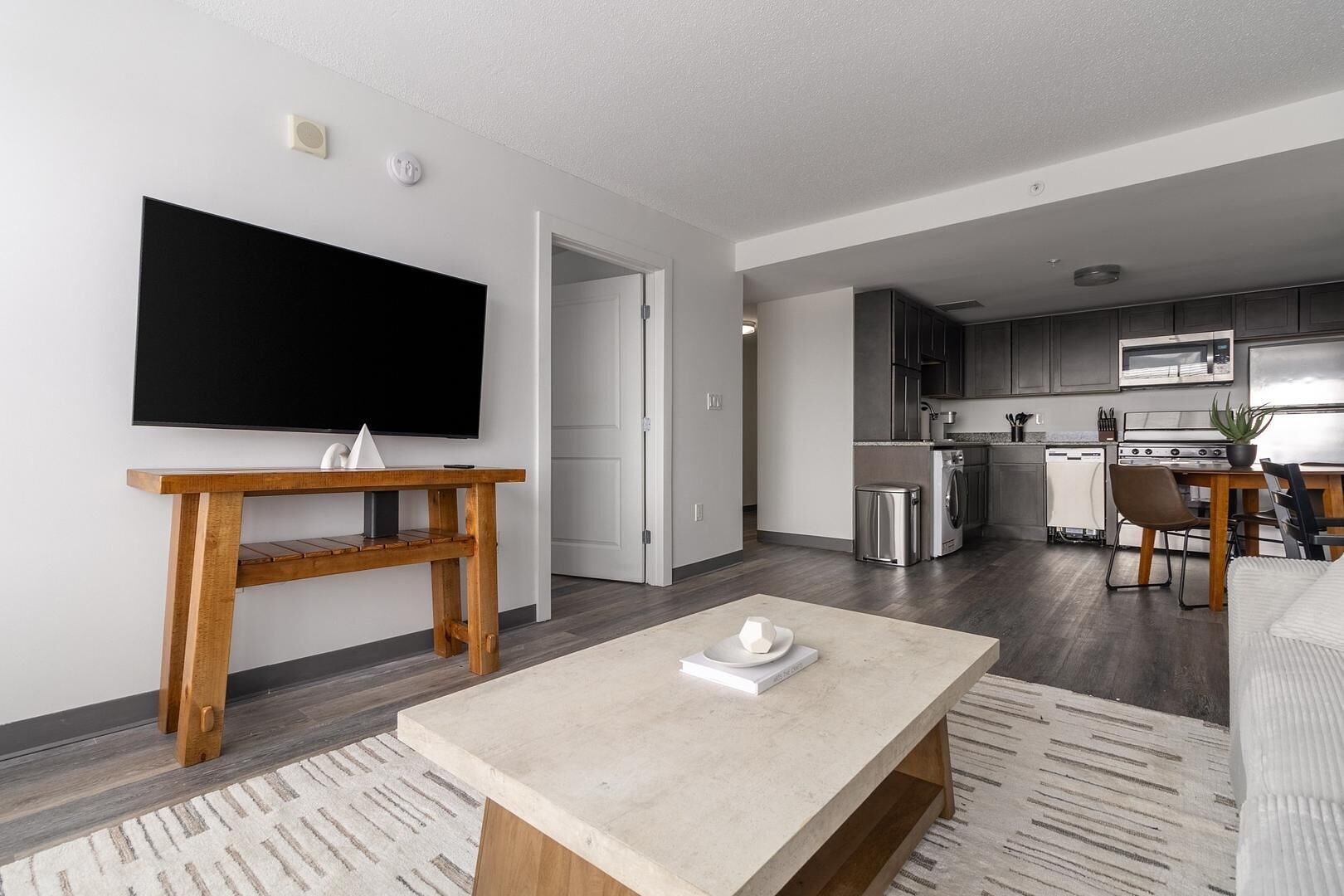 A modern living room with a flat-screen TV, wooden coffee table, and a dining area with a table and chairs.