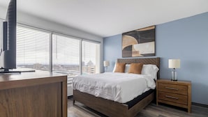 Camera d'albergo moderna con un letto grande, comodini in legno, una scrivania e vista sulla città attraverso ampie finestre a tutta parete.