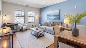 A modern living room with a sofa, coffee table, and a painting on the wall. - Landing | Incredible 2BD, Gym (Albany)