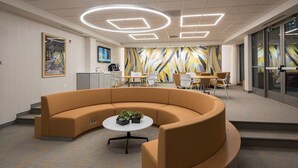 A modern waiting area with a curved sofa, a small table with plants, and a colorful geometric wall mural. - Landing | Incredible 2BD, Gym (Albany)
