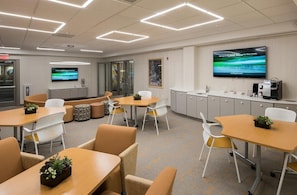 A modern office space with multiple tables and chairs, a kitchenette, and a large flat-screen TV on the wall. - Landing | Chic 2BD, Gym (Albany)
