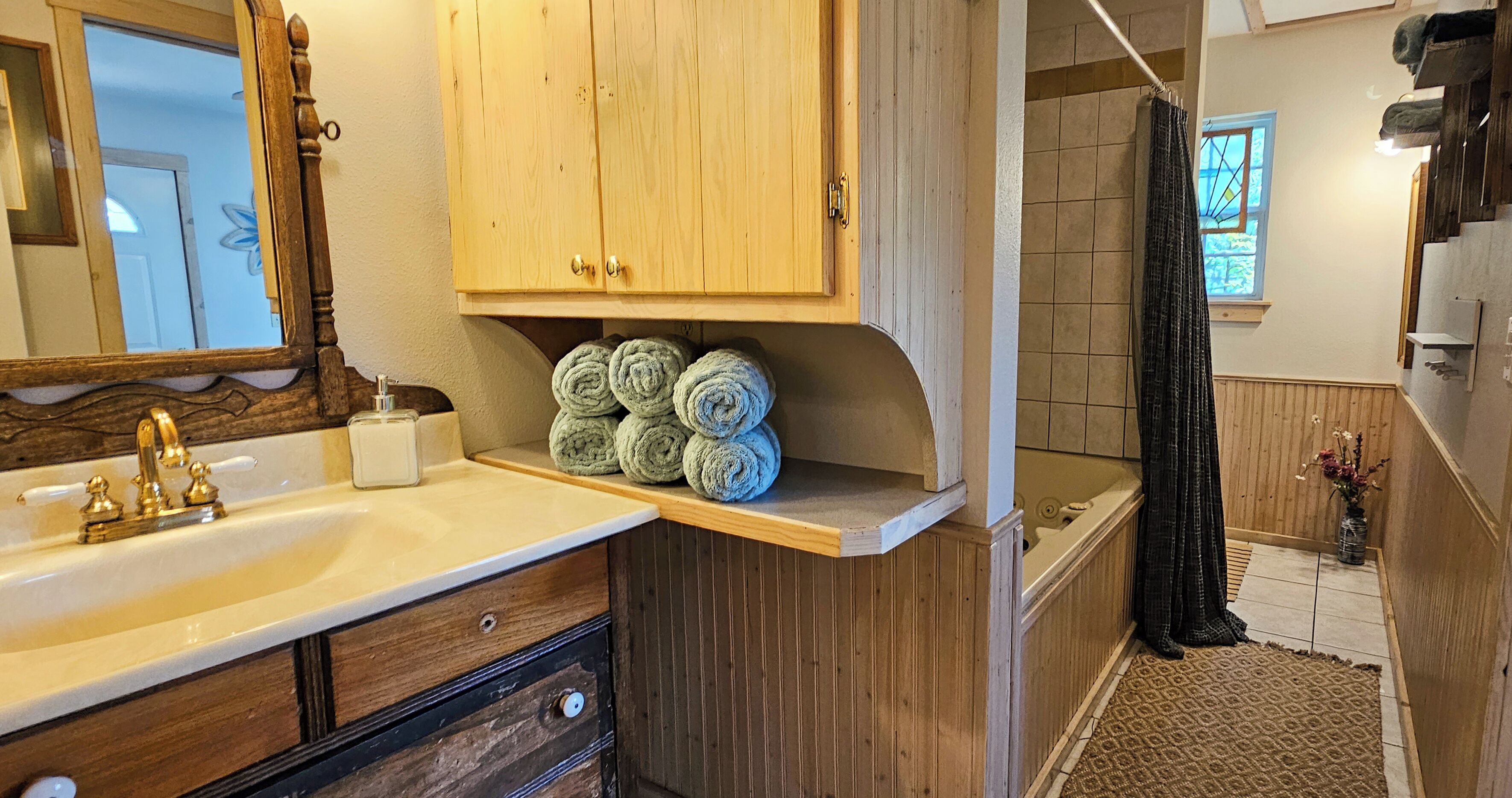A bathroom with a wooden vanity, a sink, and a shelf with rolled towels.