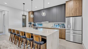 Cozinha moderna com ilha central, banquetas, eletrodomésticos de aço inoxidável e luminárias pendentes.
