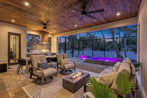 Eine geräumige Terrasse mit Feuerstelle, Sitzgelegenheiten im Freien und Blick auf ein Schwimmbad bei Einbruch der Dunkelheit.