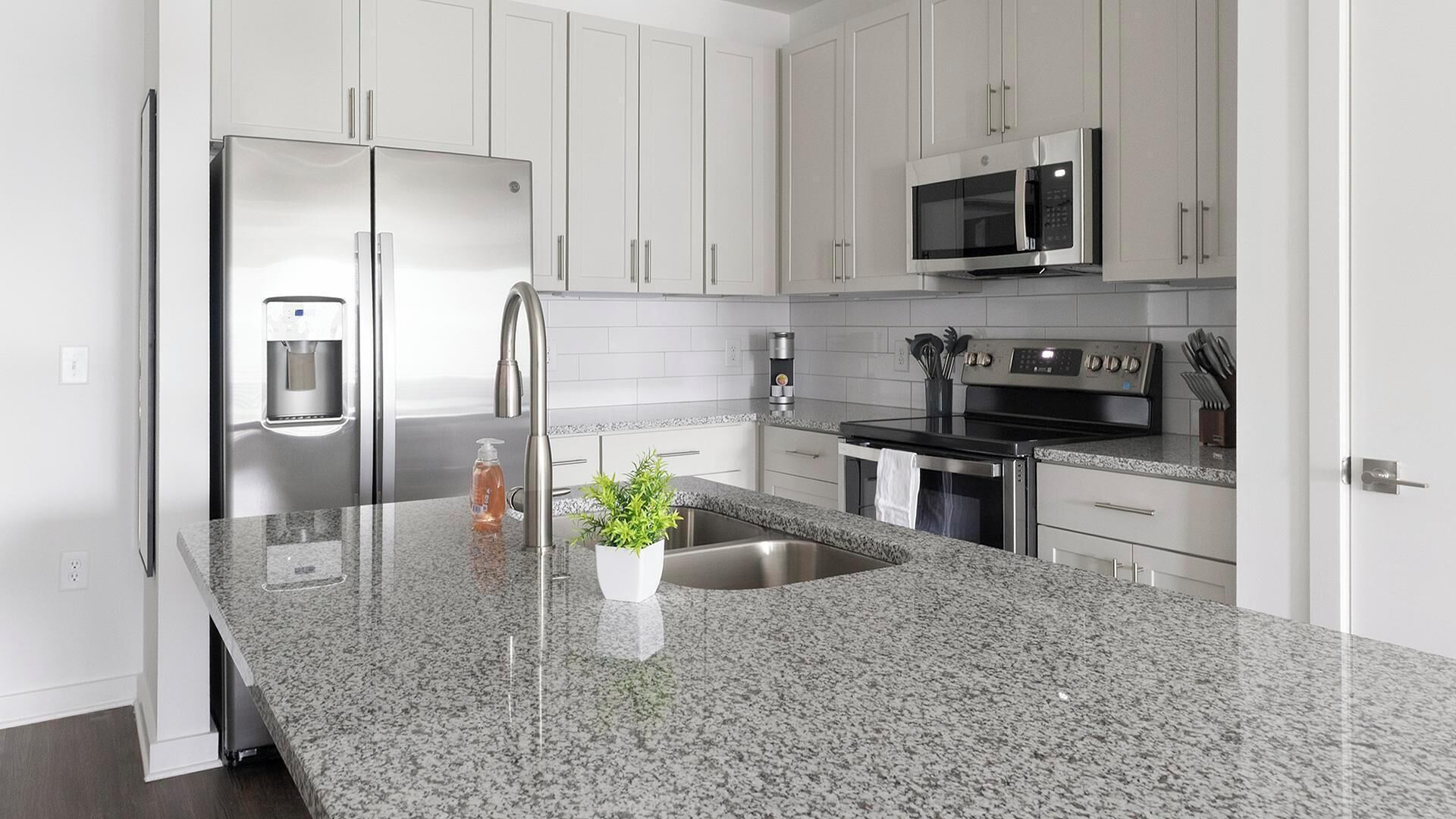 A modern kitchen with stainless steel appliances, granite countertops, and white cabinetry.