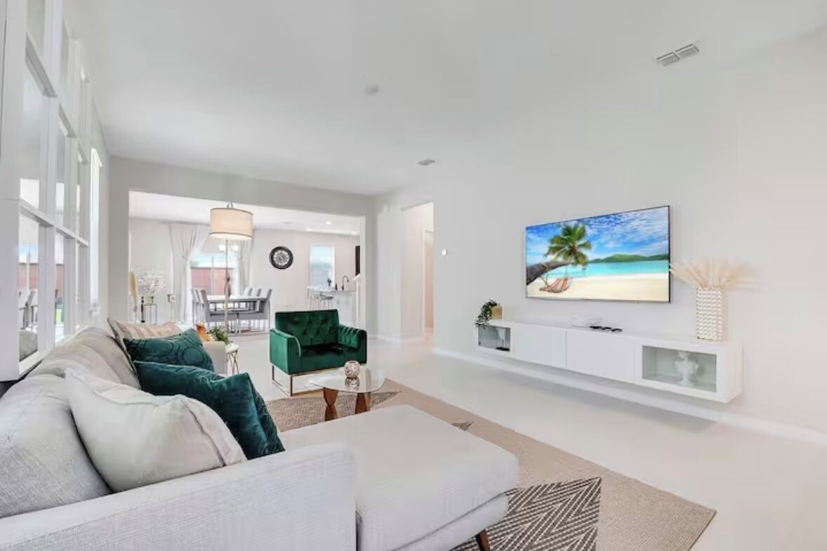 A modern living room with a large TV, a green sofa, and a white console table.