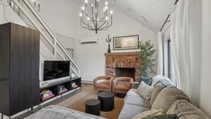 Una sala de estar moderna con una televisión, dos sillones de cuero, un sofá gris, una chimenea y una escalera.