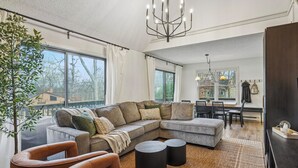 Una sala de estar moderna con un sofá seccional, sillones de cuero, un comedor con mesa y sillas, y un ventanal con vistas al exterior.