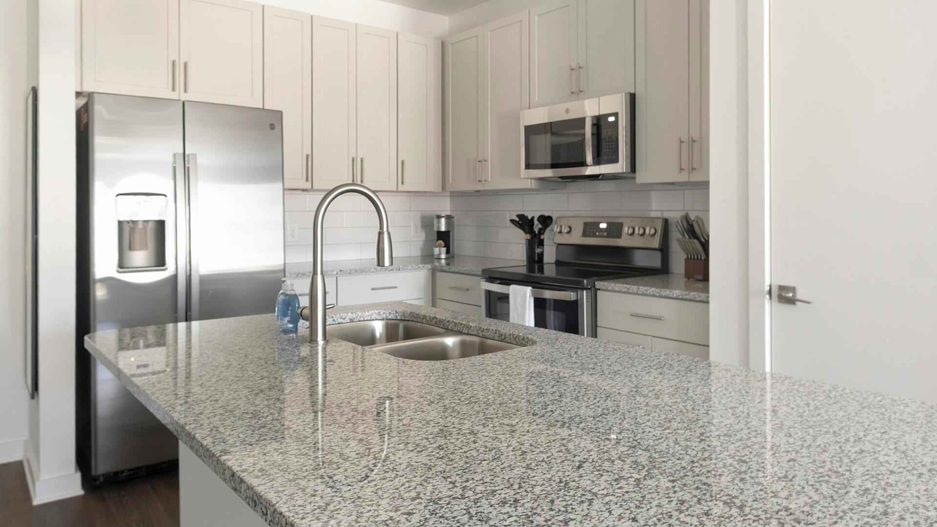 A modern kitchen with granite countertops, stainless steel appliances, and white cabinetry.