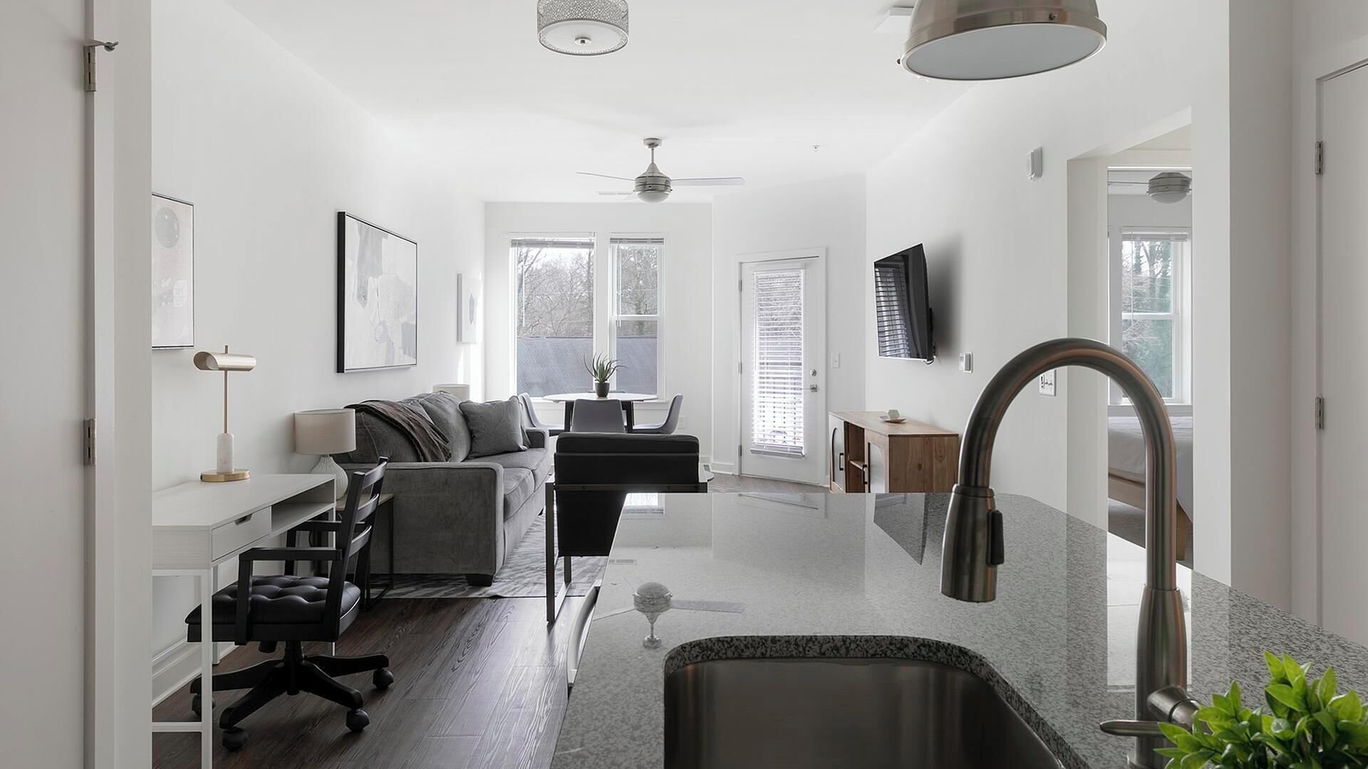 A modern kitchen with a stainless steel sink, a dining area with a sofa and chairs, and a ceiling fan.