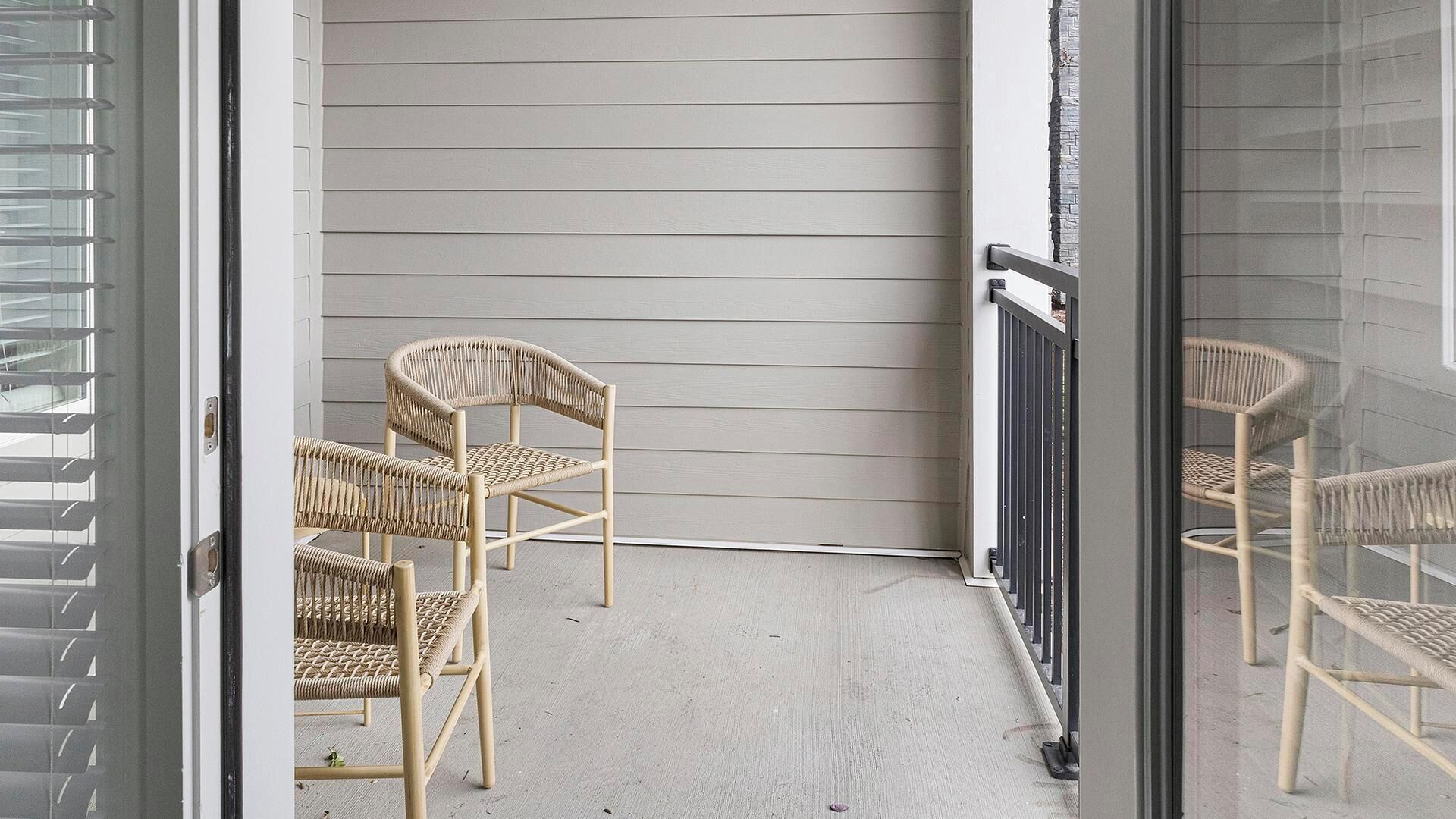 A balcony with two wicker chairs and a glass door.
