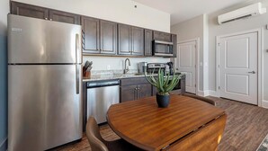 Een moderne keuken met roestvrijstalen apparatuur, donkere houten kastjes, een ingebouwde magnetron, en een eetgedeelte met een houten tafel en stoelen.