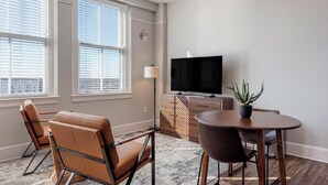 Een moderne woonkamer met een flatscreen televisie, twee leren fauteuils, een houten eettafel en een potplant.