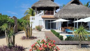 A resort with thatched-roof structures, a swimming pool, and a sandy pathway.