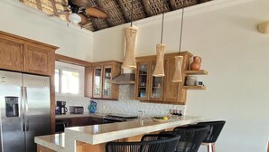A modern kitchen with wooden cabinets, a stainless steel refrigerator, a built-in oven, and a large island with bar stools.