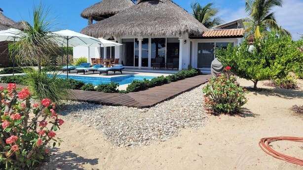 A resort with a pool, thatched-roof structures, and a sandy beach area.