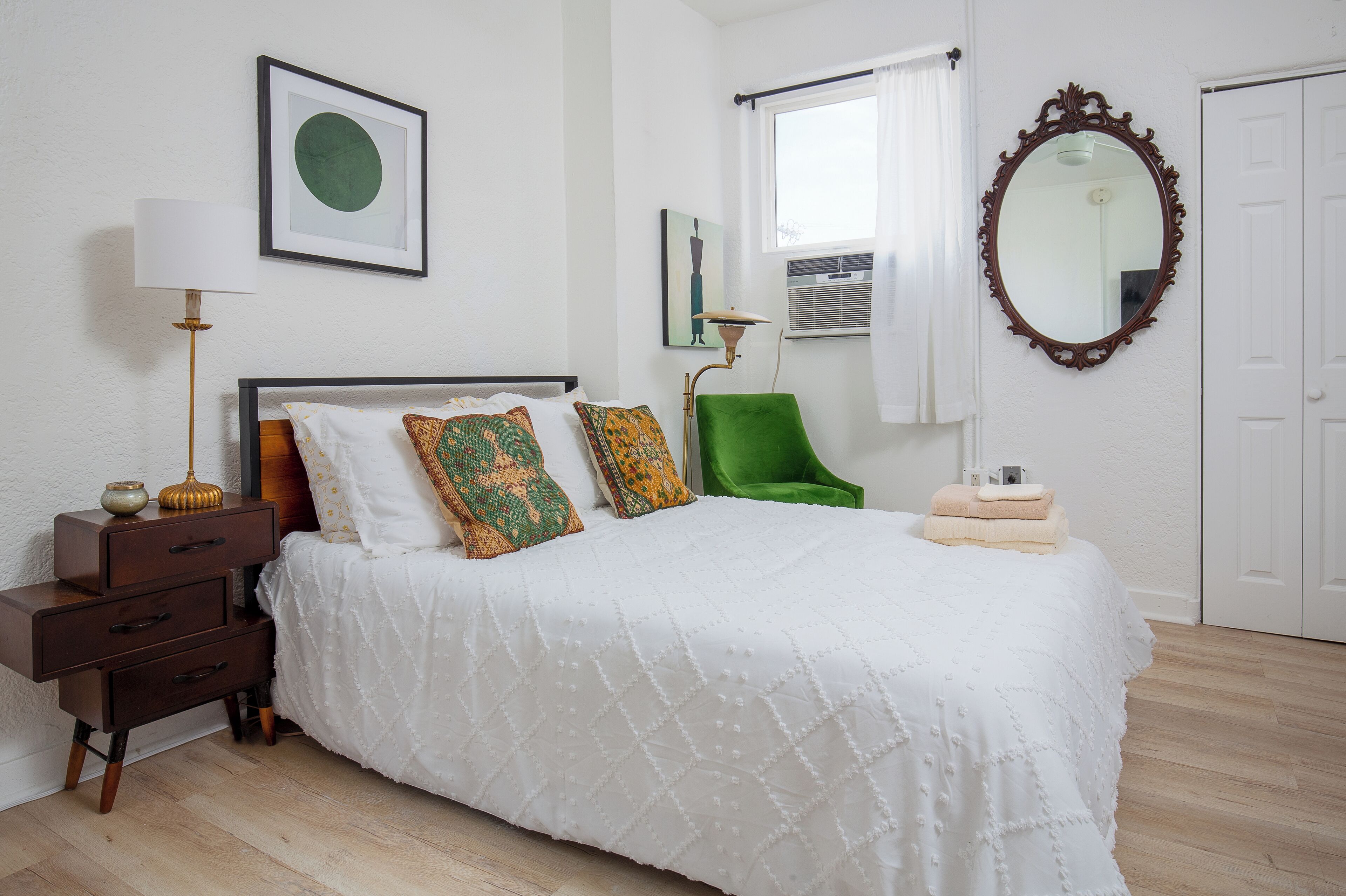 A neatly arranged bedroom with a bed, a bedside table, a lamp, a chair, and a mirror.