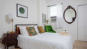A neatly arranged bedroom with a bed, a bedside table, a lamp, a chair, and a mirror. - Your cozy Studio in DTLA (Los Angeles)
