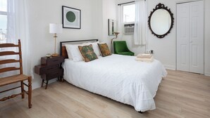 A bedroom with a bed, a chair, a nightstand, a lamp, a mirror, and a door. - Your cozy Studio in DTLA (Los Angeles)
