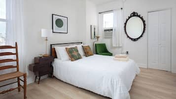 A bedroom with a bed, a chair, a nightstand, a lamp, a mirror, and a door.