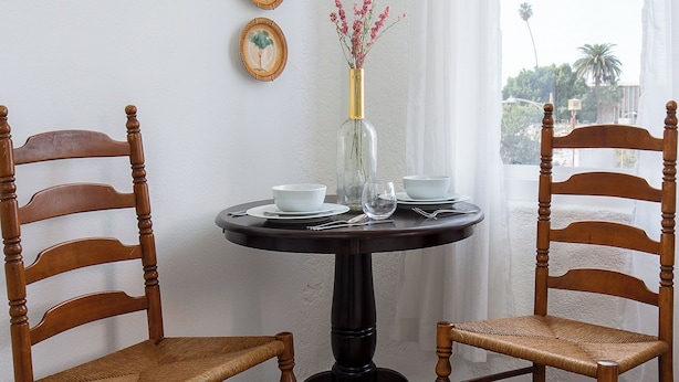 A dining area with a round table, two wooden chairs, a vase with flowers, and two wall-mounted plates. - Your cozy Studio in DTLA (Los Angeles)