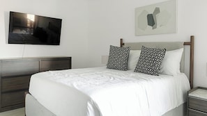 A neatly arranged bedroom with a bed, a television mounted on the wall, and a nightstand. - Landing | Chic 1BD in Uptown Charlotte (Charlotte)