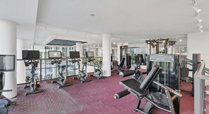 Ein modernes Fitnessstudio mit verschiedenen Trainingsgeräten, großen Fenstern und einem roten Teppich.