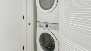 Eine weiße, übereinander gestellte Waschmaschine und Trockner mit Bedienfeld und Türgriff.