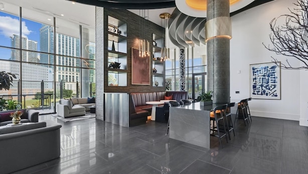 A modern interior with a seating area, a bar, and large windows offering city views. - Landing | Stylish 2BD in Uptown Charlotte (Charlotte)