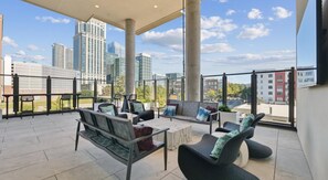 A spacious balcony with modern outdoor furniture, large windows offering a city view, and a clear sky. - Landing | Incredible 1BD in Uptown Charlotte (Charlotte)