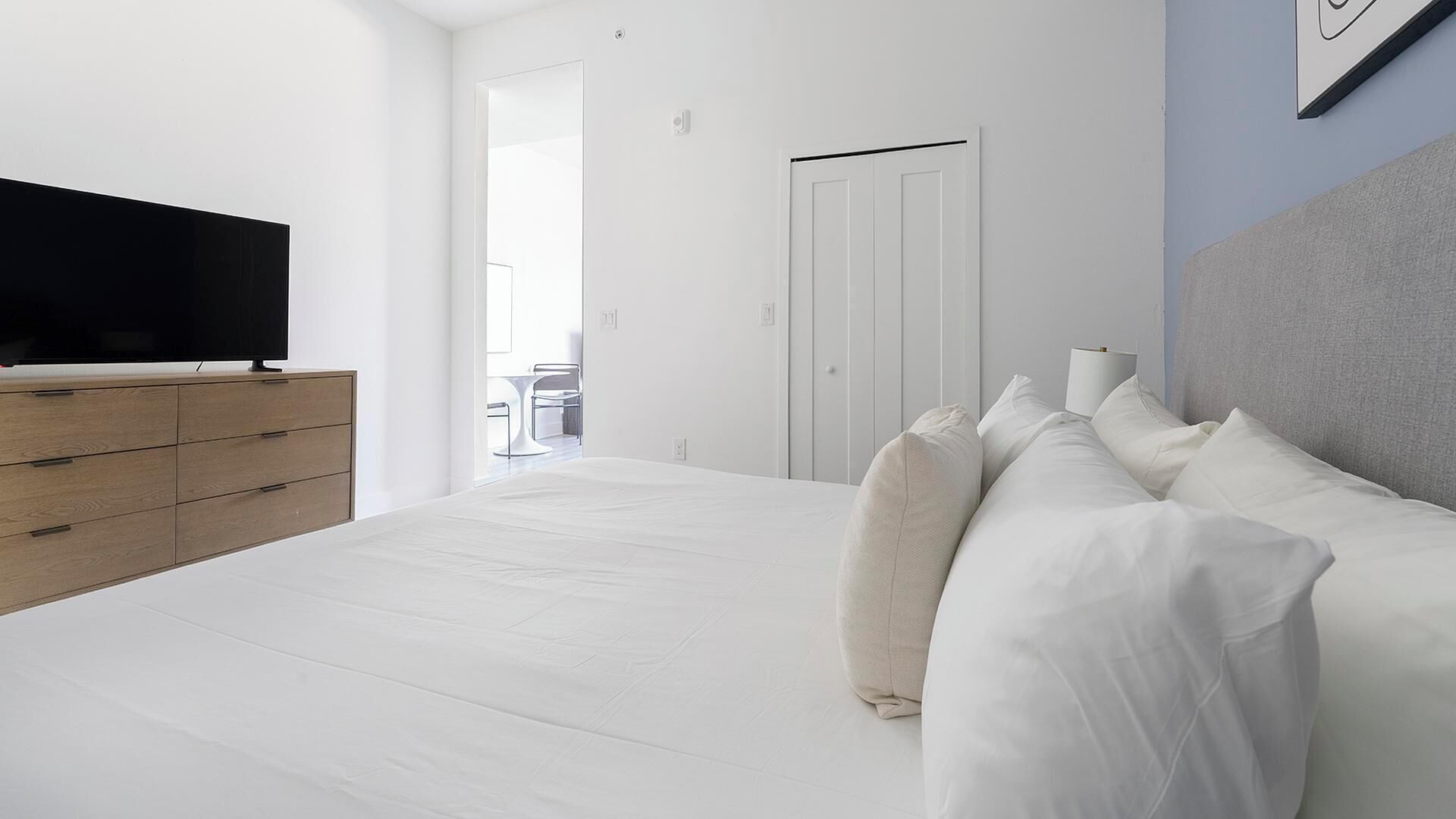 A bedroom with a bed, a TV on a wooden dresser, and a door leading to a balcony.