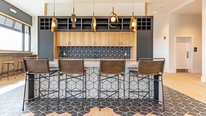 Uma cozinha moderna com armários de madeira, painel de azulejos preto e branco e um espaço de bar com banquetas de metal.