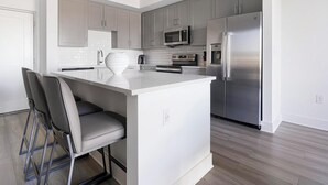 Uma cozinha moderna com armários cinzentos, eletrodomésticos de aço inoxidável, uma ilha branca com banquetas e piso de madeira.