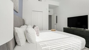 A modern bedroom with a large bed, a flat-screen TV, and a dark dresser. - Landing | Amazing 1BD, Gym, Rooftop Lounge (Fort Myers)