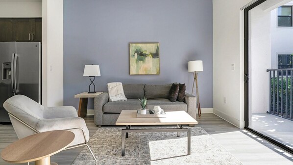 A modern living room with a grey sofa, a coffee table, and a grey armchair. There is a painting on the wall and a floor lamp. - Landing | Amazing 1BD, Gym, Rooftop Lounge (Fort Myers)