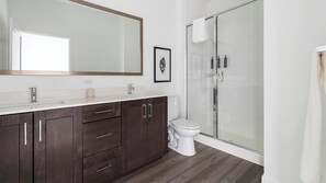 A modern bathroom with a dark wood vanity, a large mirror, a white toilet, and a glass shower enclosure. - Landing | Amazing 1BD, Gym, Rooftop Lounge (Fort Myers)