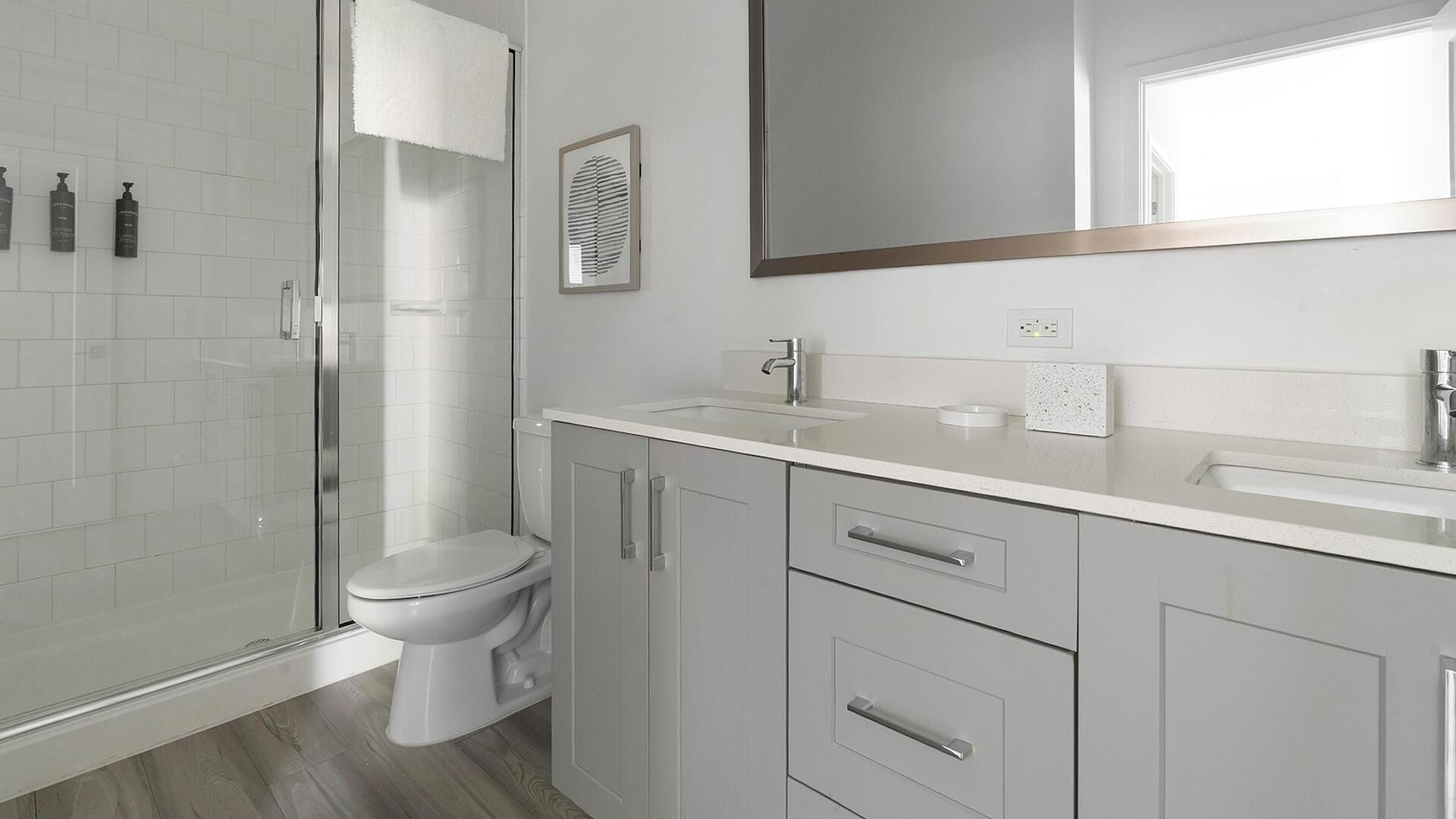 Un baño moderno con cabina de ducha de vidrio, inodoro, lavamanos y espejo.