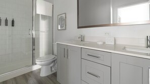 A modern bathroom with a glass shower enclosure, a toilet, a sink, and a mirror. - Landing | Stunning 1BD, Gym, Game Room (Fort Myers)