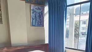 A hotel room with a bed, a window with blue curtains, and a painting on the wall. - Samana Wasi Urpicha (Cusco)
