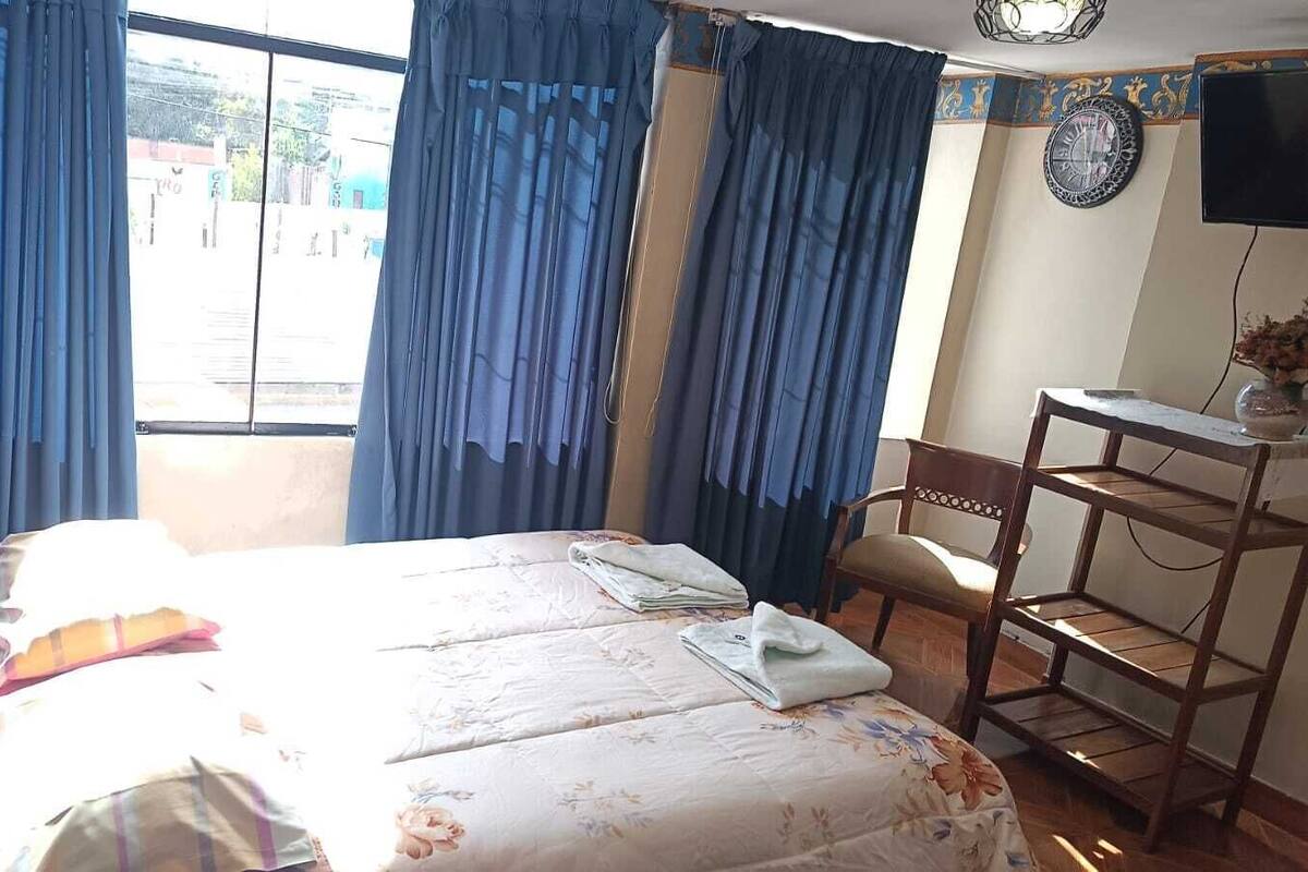 A bedroom with a bed, a chair, a desk, and a window with curtains.