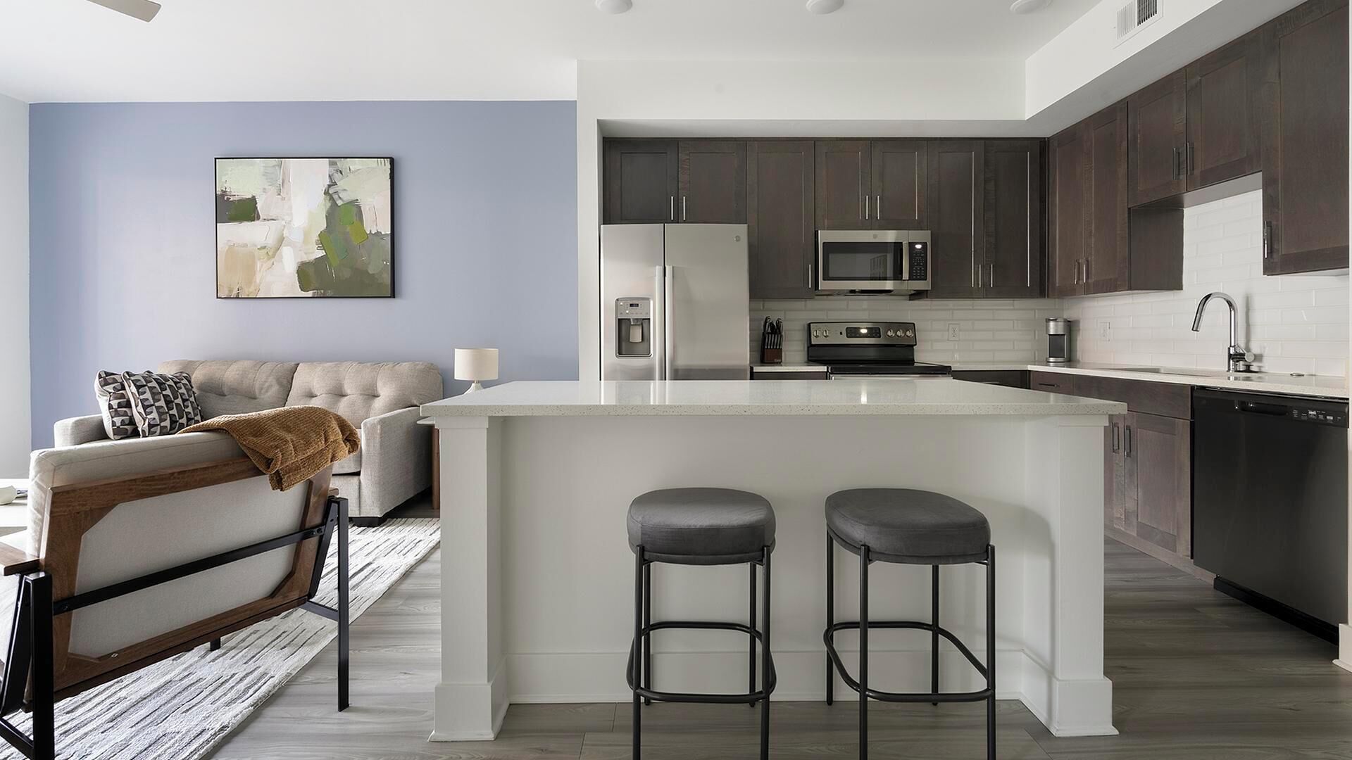 A modern kitchen with dark cabinets, a central island with stools, a microwave, and a refrigerator.