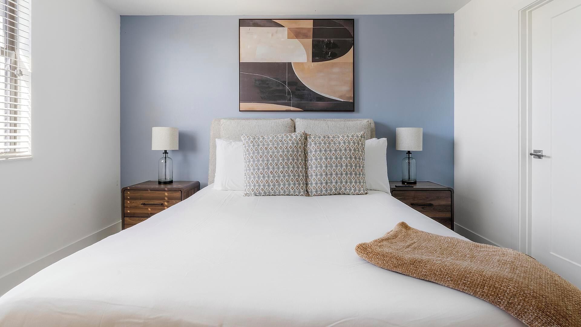 A bedroom with a large bed, two bedside tables, a wall art piece, and a door.