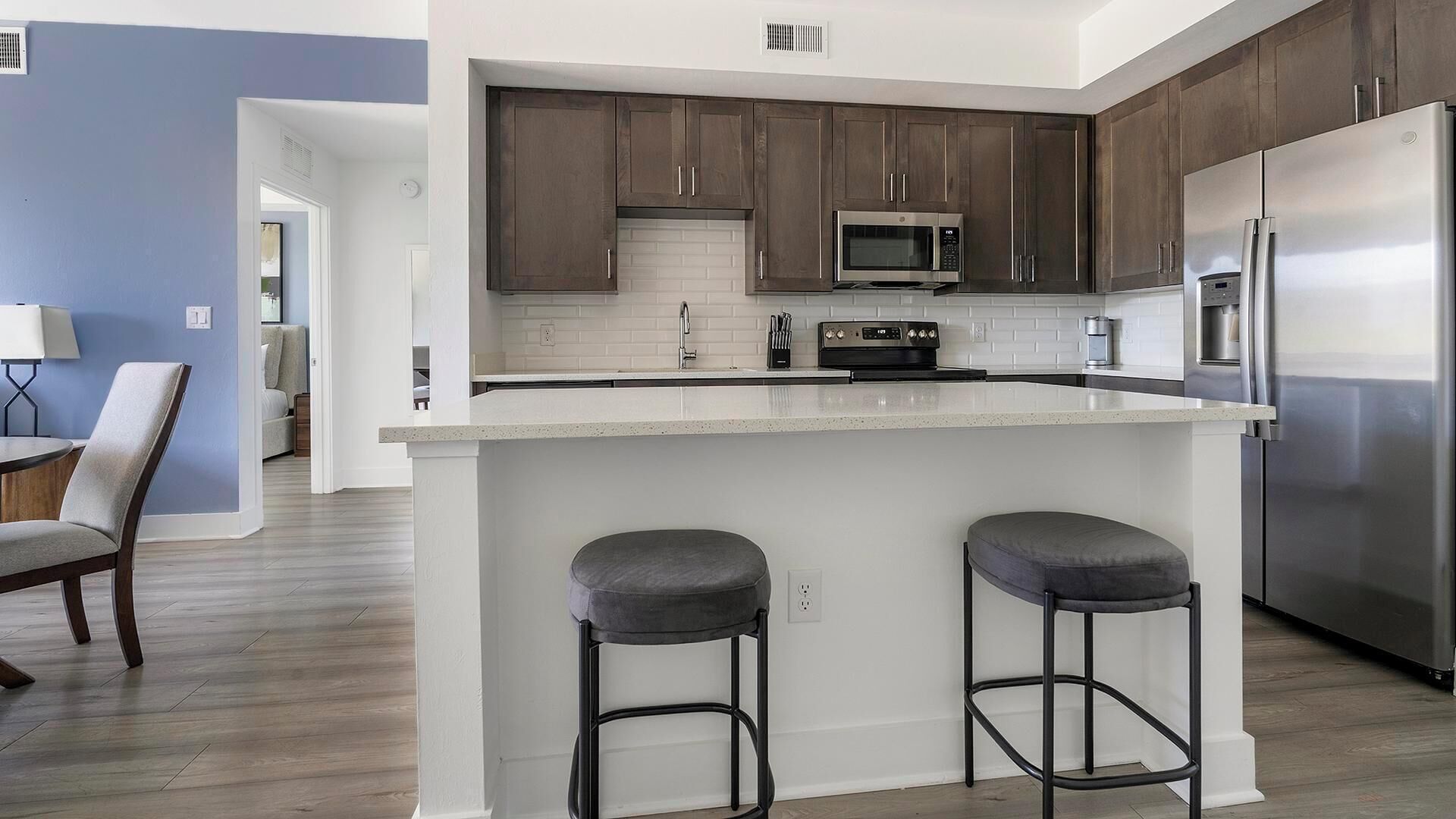 Una cocina moderna con armarios de madera oscura, electrodomésticos de acero inoxidable y una isla central con taburetes de bar.