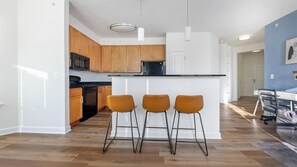 Eine moderne Küche mit Holzausstattung, einer schwarzen Arbeitsplatte und drei Barhocker.