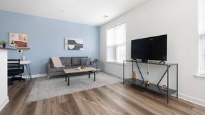 Un salon moderne avec un canapé gris, une table basse, un téléviseur posé sur un meuble noir et un tableau accroché au mur.
